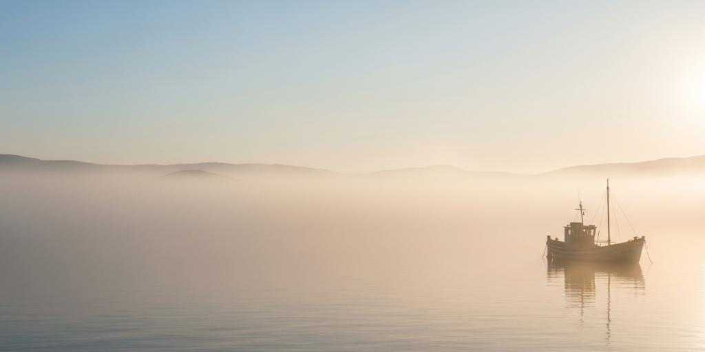 A small fishing boat navigating through thick morning mist on a calm sea at sunrise, representing the careful navigation and strategic planning required for a successful market entry.