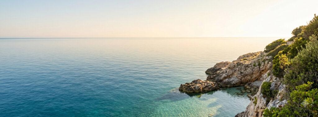 Tranquil Mediterranean coastline featuring clear turquoise water, rocky cliffs covered in lush green vegetation, and bright sunlight setting a summer vibe for field research stories.